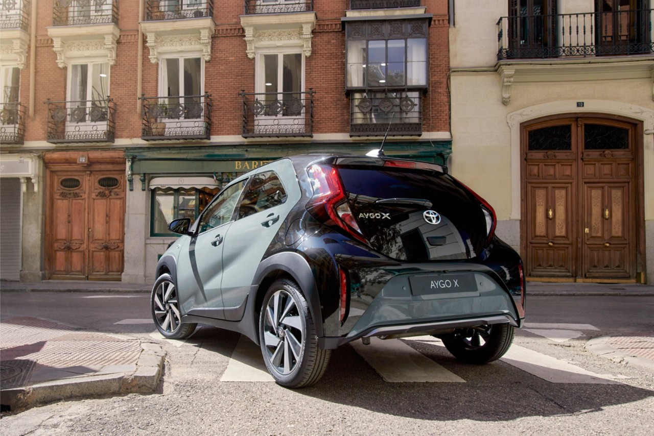 Image showin gthe tarragon Green Aygo X driving away around a corner in the city